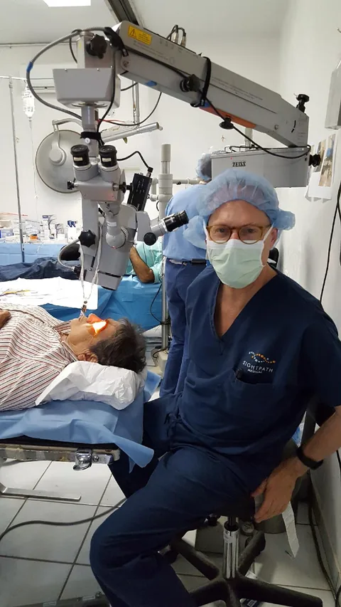 Dr. Perlman in scrubs beside a surgical microscope on a mission trip