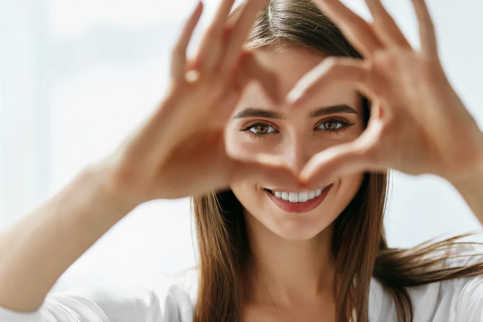 Smiling woman making a heart shape with her hands around her eyes